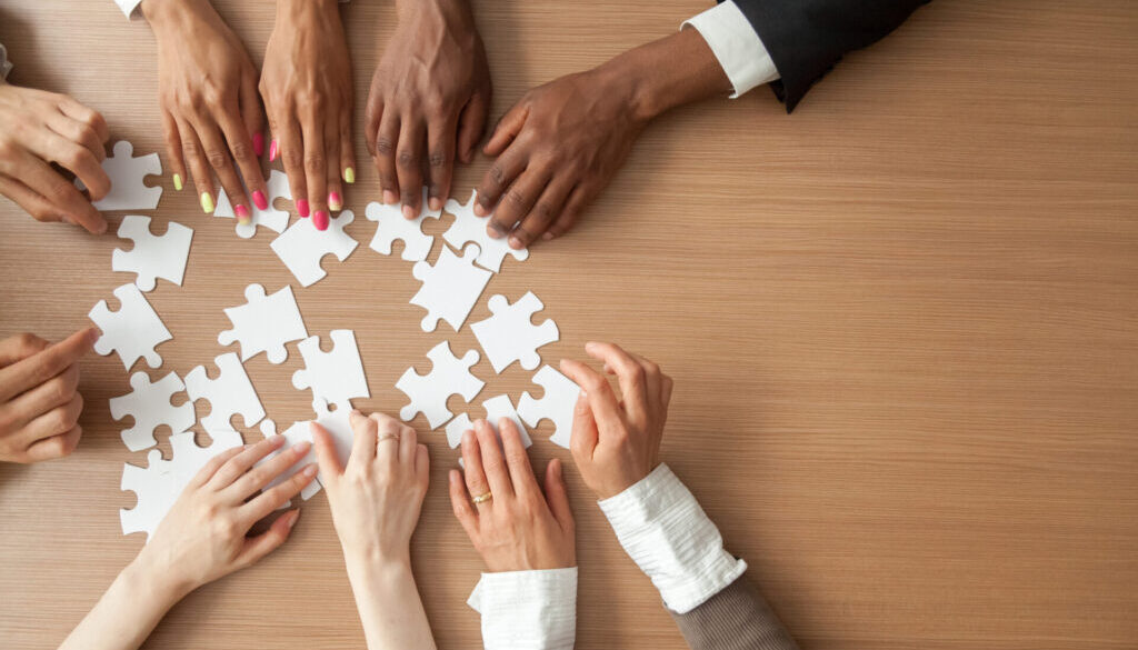 Hands of multi-ethnic team assembling jigsaw puzzle, multiracial group of black and white people joining pieces at desk, successful teamwork concept, help and support in business, close up top view practicing networking best practices